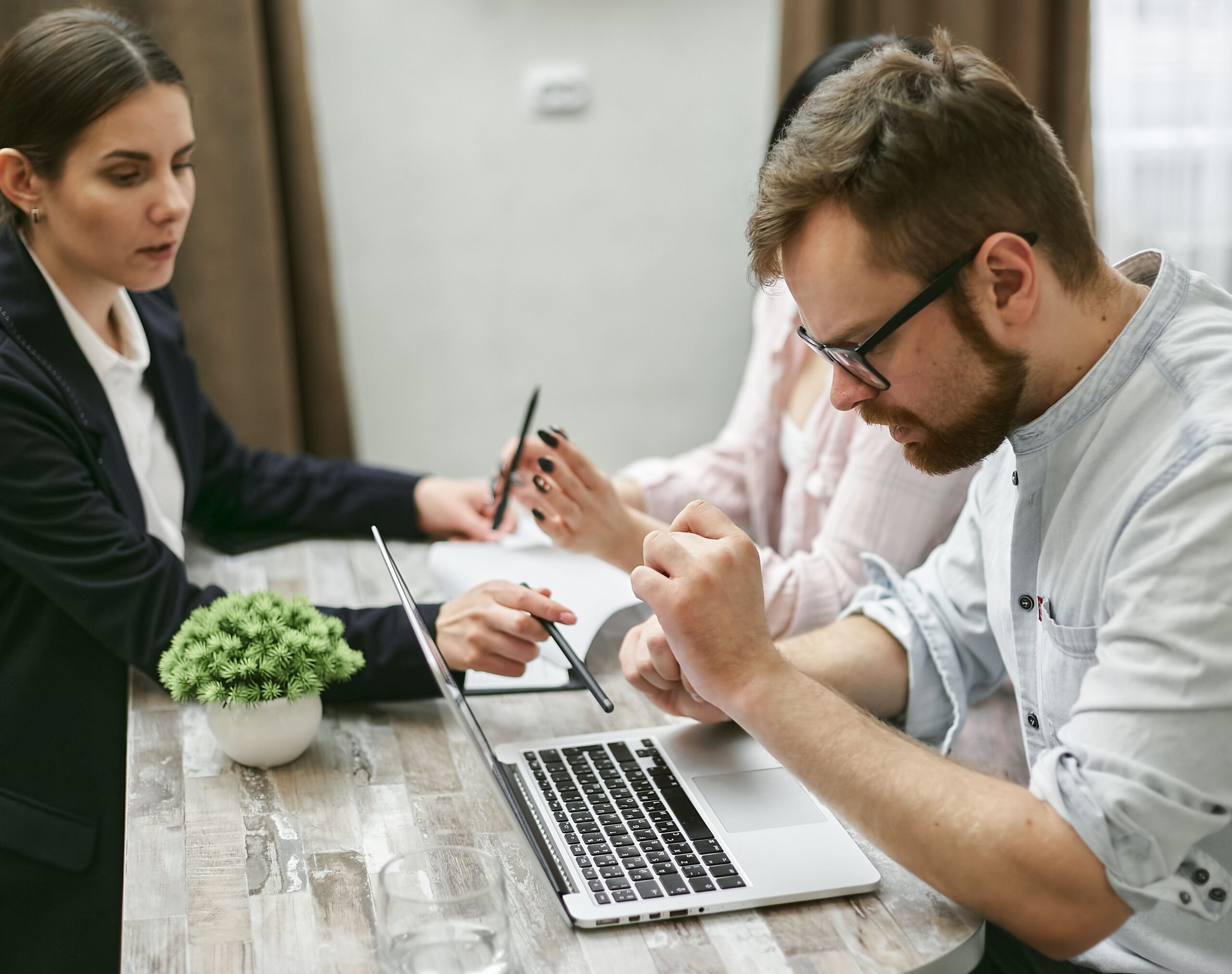 Three professionals engage in a collaborative meeting, discussing ideas over a laptop in an office setting.